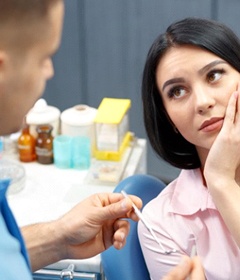 A woman holding her mouth while listening to a dentist.