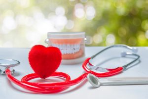 Red heart shape sitting next to model teeth and stethoscope 