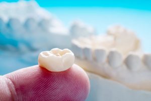 dental crown on the fingertip of dentist model teeth in background