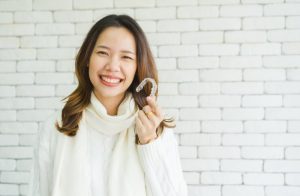 a woman smiling with an aligner in her hand