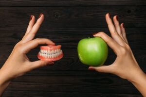 Person hold dentures in one hand and an apple in the other