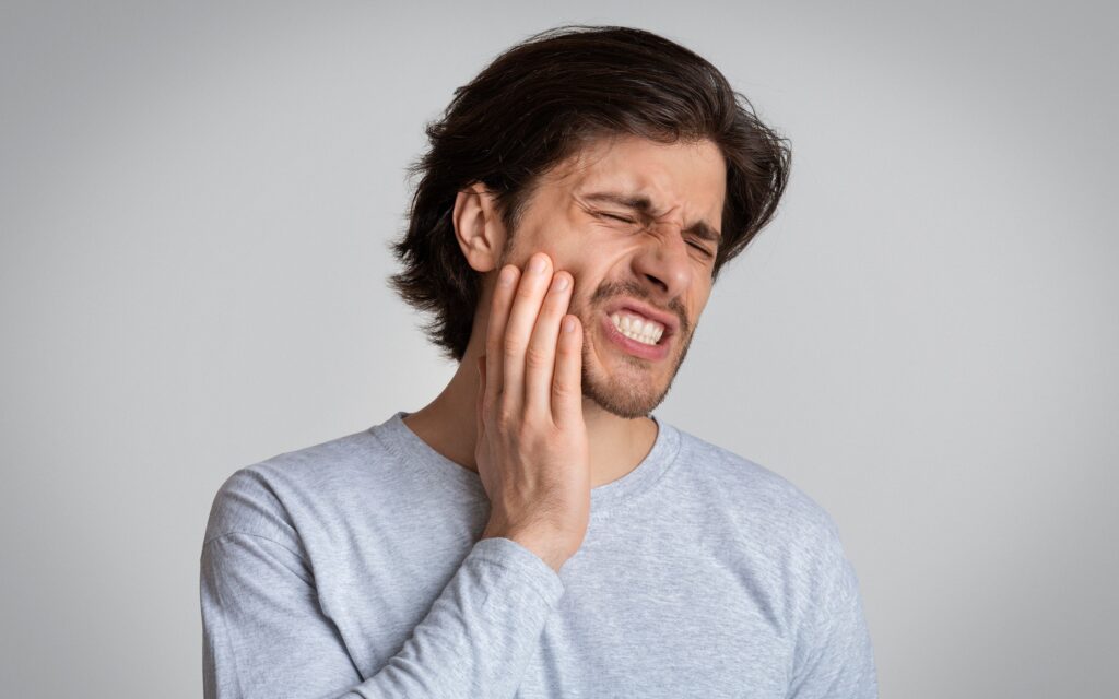 Man in gray shirt holding hand to jaw in pain