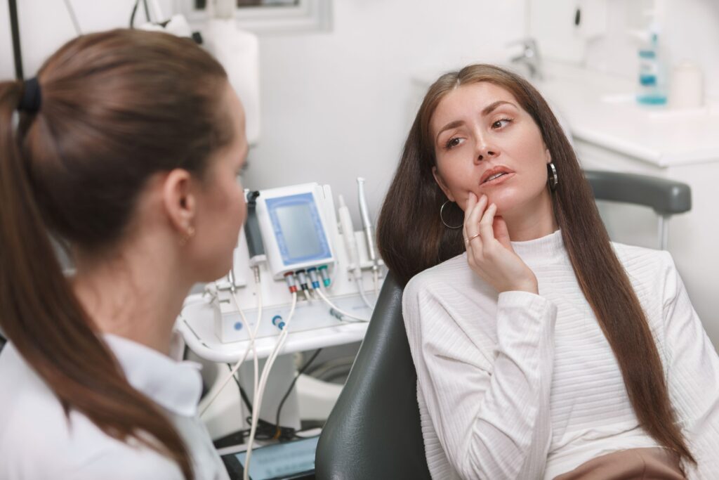 Woman in dental chair touching cheek in pain