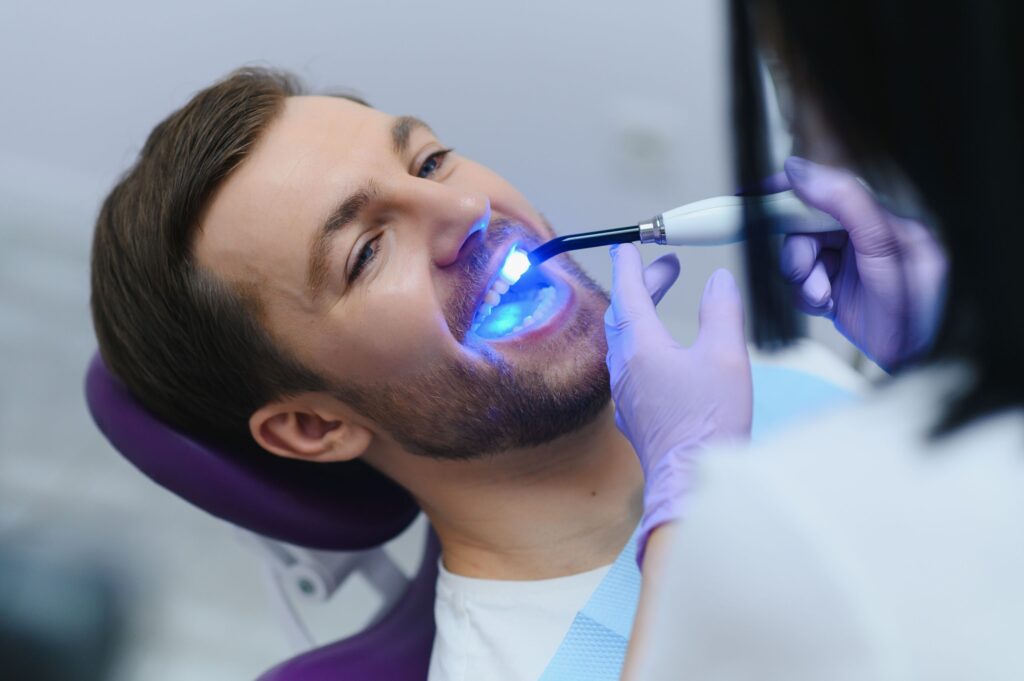 Dentist using UV light to harden a man's dental bonding