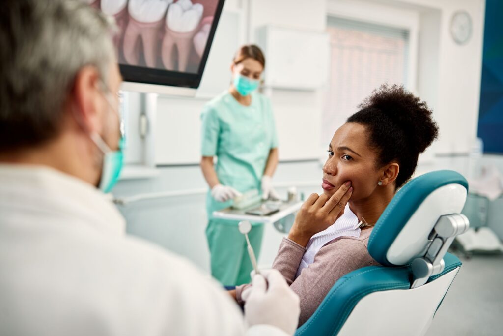 Woman in dental chair touching jaw to tell dentist where it hurts